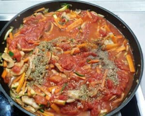 Gemüse mit gehackten Tomaten und Gewürzen in einer Pfanne.