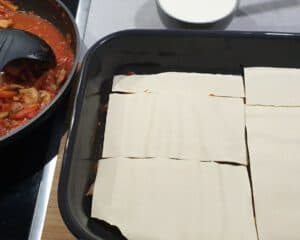 Lasagne Platten auf einer Soße in einer Auflaufform.