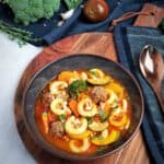 Minestrone - italienische Gemüse-Suppe angerichtet in einer braunen Schale. Im Hintergrund Deko.