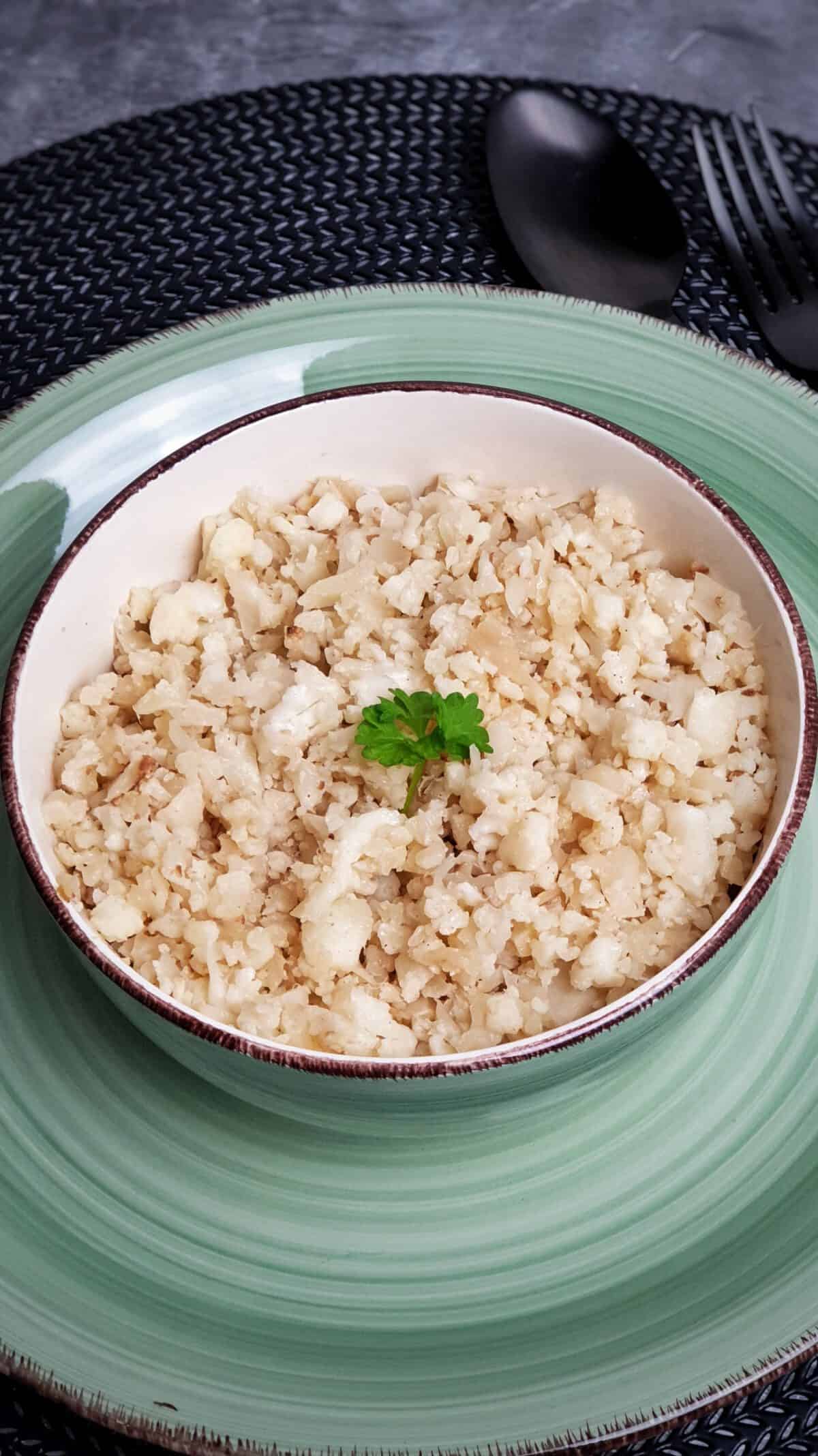 In einer hellen Schale auf einem grünen Teller angebratenen Blumenkohlreis, schneller Low Carb Reis mit etwas Petersilie als Deko.