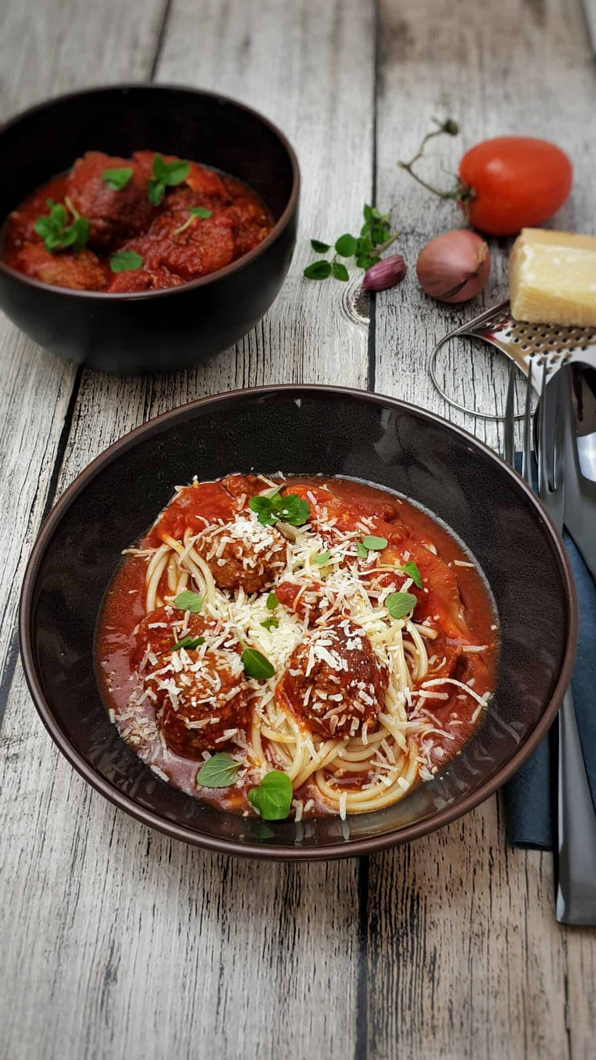 In einer braunen Schüssel Hackfleisch-Bällchen mit Tomatensoße und Spaghetti. Serviert mit Parmesan und frischem Oregano.