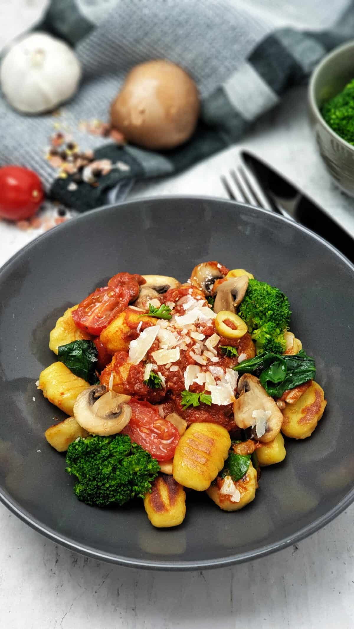 Gnocchi mit Tomatensoße und Gemüse in einer grauen Schale angerichtet.