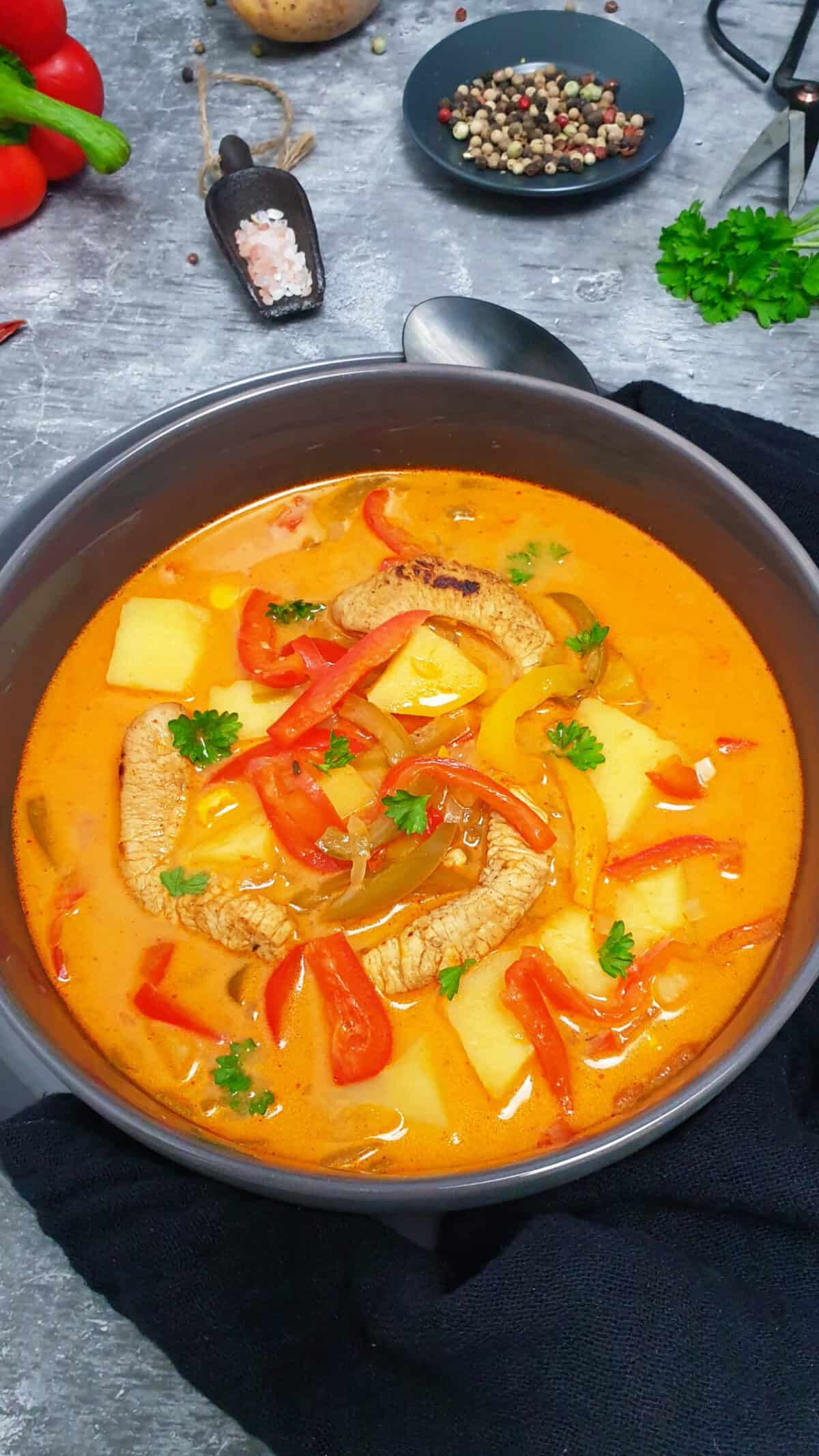 In einer grauen Schale eine Suppe mit Gyros-Fleisch, Paprika und Kartoffeln. Im Hintergrund Deko.